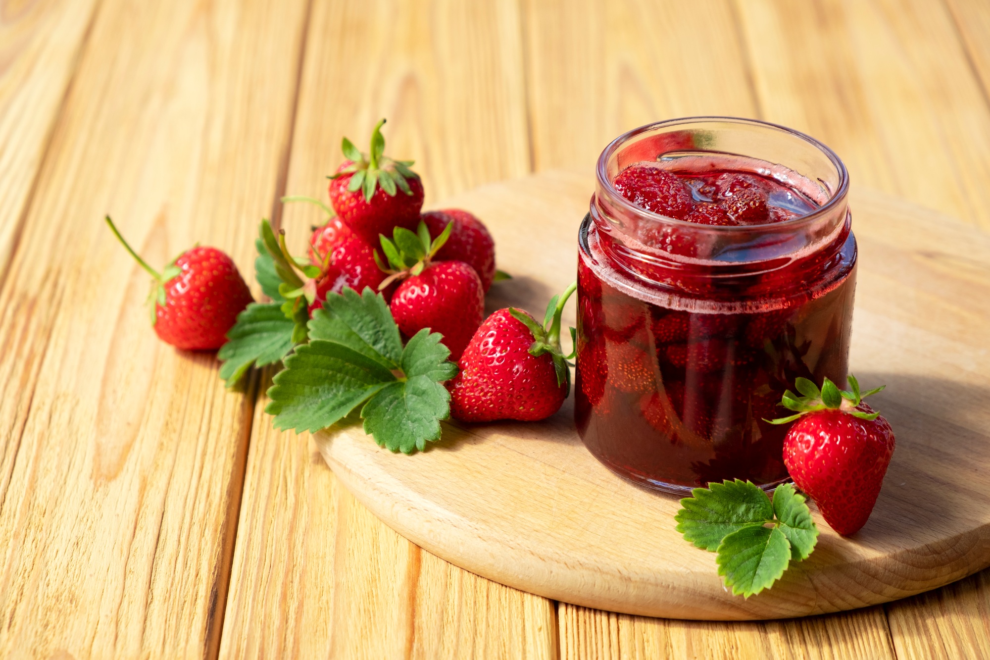 Strawberry jam in glass jar on wooden board.