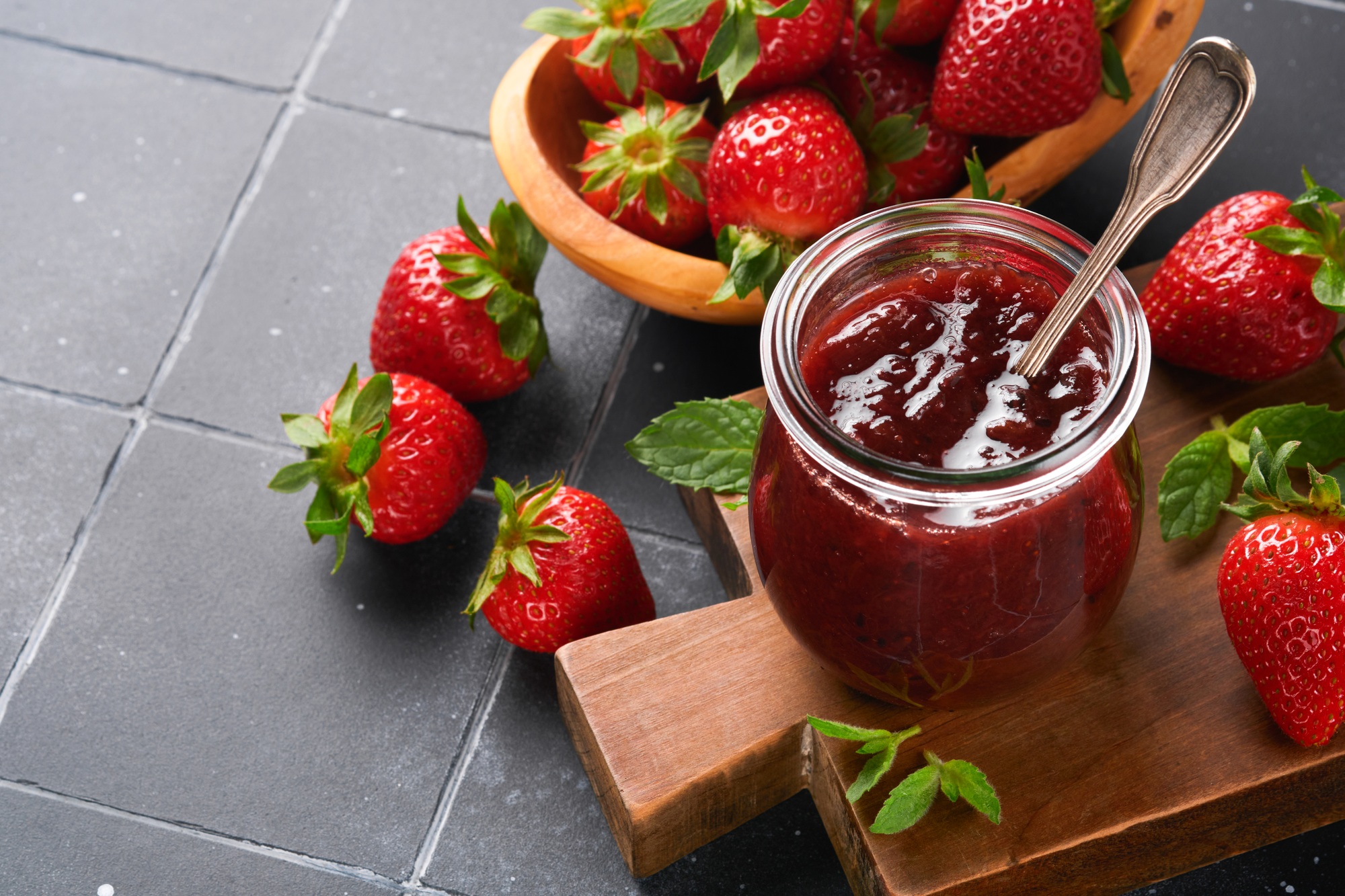 Strawberry jam. Strawberry jam in glass jar with fresh berries plate on an old black cracked tile ta